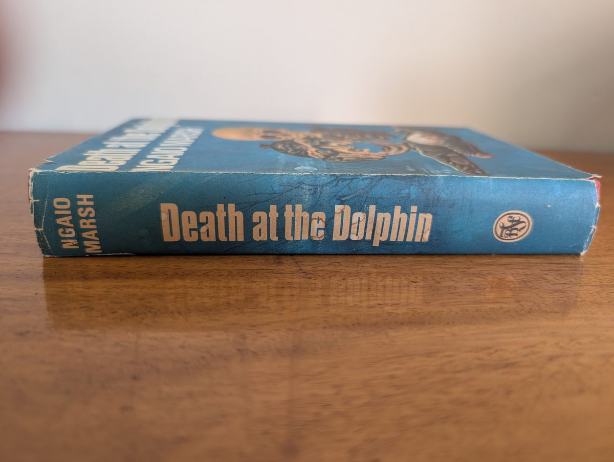 A photograph of the spine of the 1967 Collins Crime Club hardback edition of Ngaio Marsh's Death at the Dolphin. It shows some tearing at the top and bottom of the dust jacket.