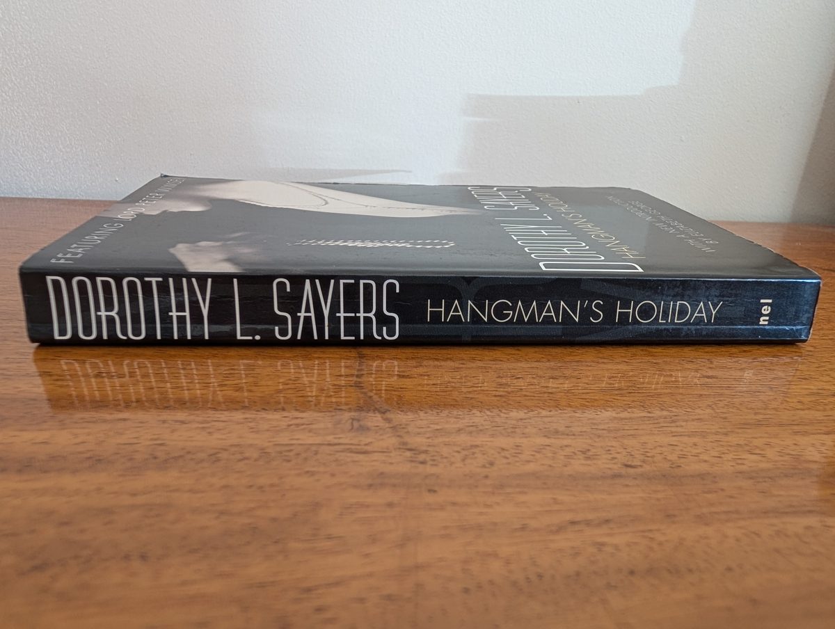 The spine of the 1974 New English Library paperback of Hangman's Holiday by Dorothy L. Sayers, photographed lying flat. The black spine shows 'DOROTHY L. SAYERS / HANGMAN'S HOLIDAY' in white type with the NEL logo at one end.