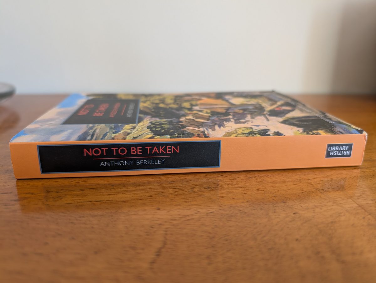 The spine of the 2025 British Library Crime Classics paperback of Not To Be Taken by Anthony Berkeley, photographed lying flat on a wooden surface. The orange spine has a dark rectangular panel with the title in red lettering and 'ANTHONY BERKELEY' in white. The British Library logo appears at the right-hand end.