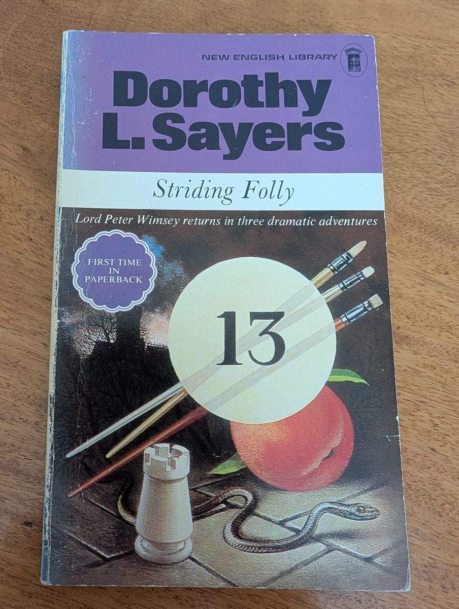 The front cover of the 1972 first New English Library paperback edition of Striding Folly by Dorothy L. Sayers. The cover features a surrealist still-life illustration showing a large white billiard ball with the number 13, several paintbrushes, a chess rook, a coiled snake, and a peach against a dark background. 'DOROTHY L. SAYERS' appears in large purple type at the top, 'Striding Folly / Lord Peter Wimsey returns in three dramatic adventures' below, with a circular sticker reading 'FIRST TIME IN PAPERBACK'.