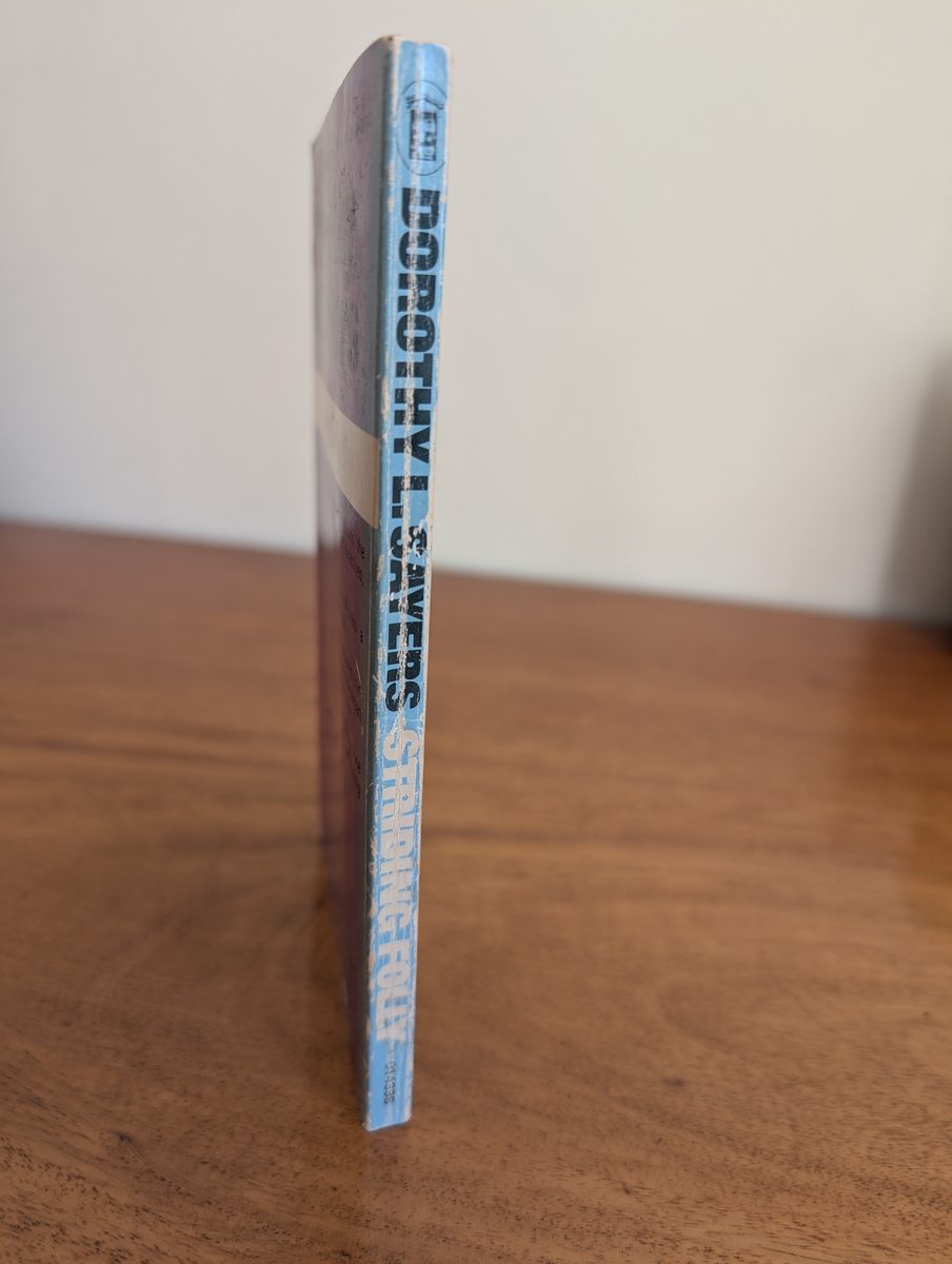 The spine of the 1972 first New English Library paperback of Striding Folly by Dorothy L. Sayers, photographed standing upright. The blue-lavender spine shows 'DOROTHY L. SAYERS / STRIDING FOLLY' with the NEL logo at the top. Significant fading and creasing are visible, consistent with the book's age.