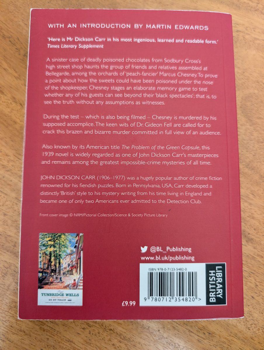 The back cover of the 2023 British Library Crime Classics paperback of The Black Spectacles by John Dickson Carr. The red background carries a Times Literary Supplement quote, a plot synopsis, a biographical note on Carr, social media handles, a small thumbnail of a vintage Tunbridge Wells travel poster, and an ISBN barcode. Priced at £9.99.