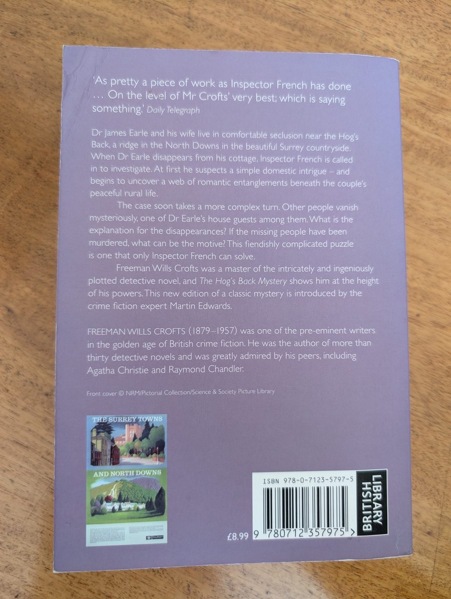 The back cover of the 2015 British Library Crime Classics paperback of The Hog's Back Mystery by Freeman Wills Crofts. The lavender background carries a Daily Telegraph quote, a plot synopsis, and a biographical note on Crofts, along with small thumbnails of vintage railway posters for Surrey and the North Downs. ISBN barcode and price of £8.99.