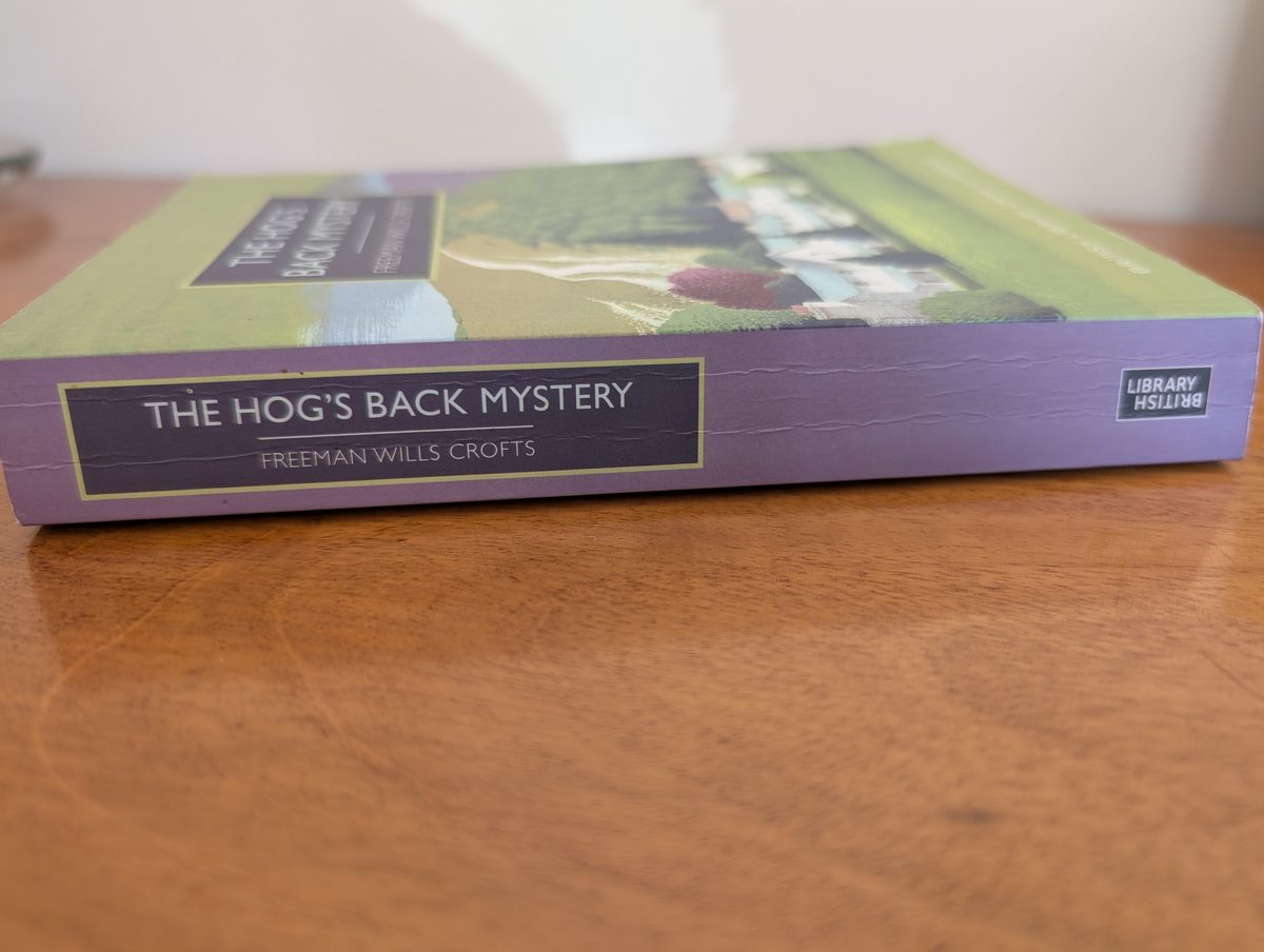The spine of the 2015 British Library Crime Classics paperback of The Hog's Back Mystery by Freeman Wills Crofts, photographed lying flat. The lavender spine shows a dark navy panel with 'THE HOG'S BACK MYSTERY' and 'FREEMAN WILLS CROFTS' in silver lettering with gold borders. The British Library logo appears at one end.
