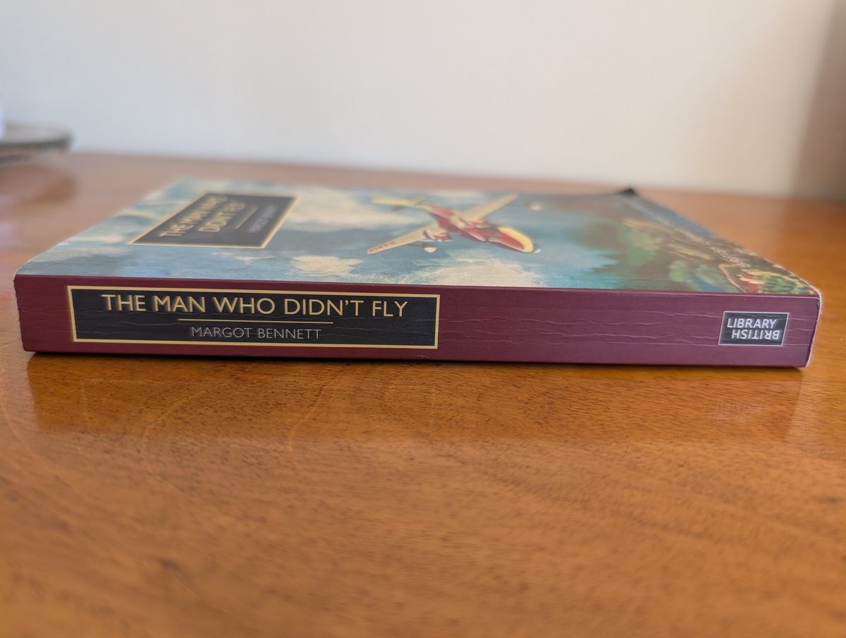 The spine of the 2020 British Library Crime Classics paperback of The Man Who Didn't Fly by Margot Bennett, photographed lying flat. The deep plum spine shows a dark panel with 'THE MAN WHO DIDN'T FLY' and 'MARGOT BENNETT' in gold lettering with gold borders. The British Library logo appears at one end.