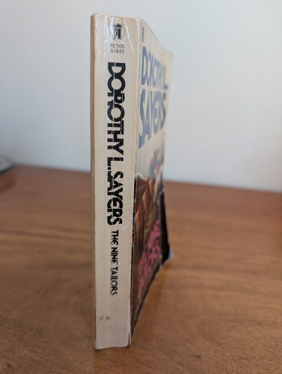 The spine of the 1982 New English Library paperback of The Nine Tailors by Dorothy L. Sayers, photographed standing upright. The cream and white spine shows 'DOROTHY L. SAYERS / THE NINE TAILORS' in black type with the NEL logo at the top. Light creasing and yellowing are visible.
